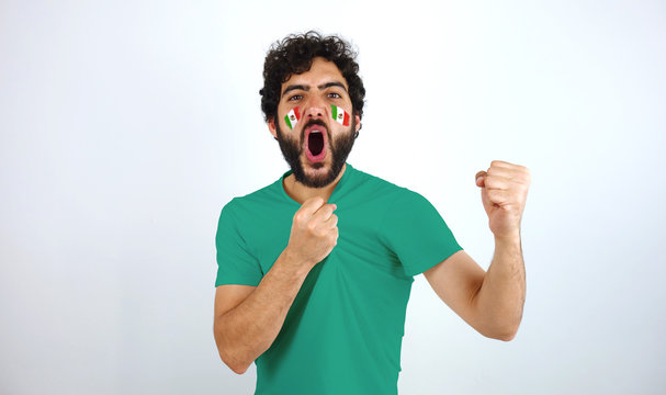 Sport fan screaming for the triumph of his team. Man with the flag of Mexico makeup on his face and green t-shirt.