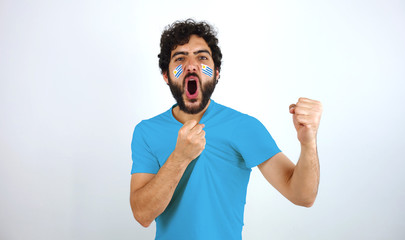 Sport fan screaming for the triumph of his team. Man with the flag of Uruguay makeup on his face and blue t-shirt.