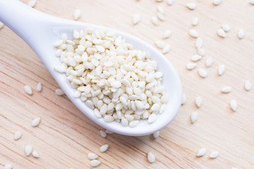 The white sesame on the white ceramic spoon are placed  the wooden table.