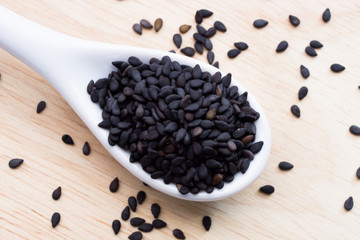 The black sesame on the white ceramic spoon are placed  the wooden table.