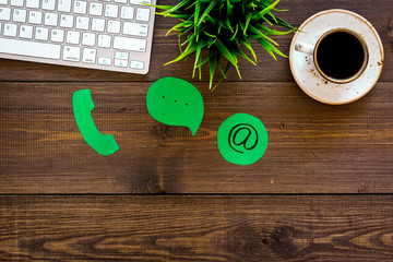 Customer service concept. Concact information. Phone, message, email signs on office work desk with computer on dark wooden background top view copy space