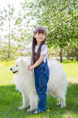 Little girl with a big white dog in the park. A beautiful 5 year old girl in jeans hugs her favorite dog during a summer walk.