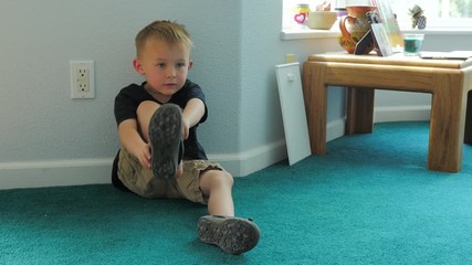 3 year old boy puts on some shoes before going out to play.