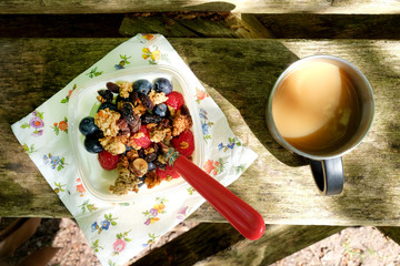 muesli cereal with fruit and yogurt in a bowl with coffee on wooden table