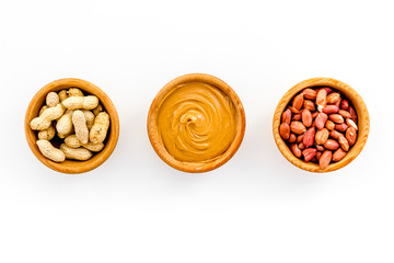 Peanut paste concept. Bowls with butter, nuts in shell, peeled nuts on white background top view copy space