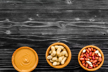 Peanut paste concept. Bowls with butter, nuts in shell, peeled nuts on black wooden background top view copy space
