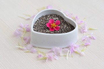 Obraz na płótnie Canvas Chia seeds (Salvia hispanica) in ceramic bowl of heart shape, decorated with flowers