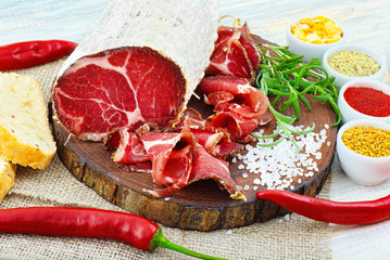 Sliced cured coppa with spices and a sprig of rosemary.