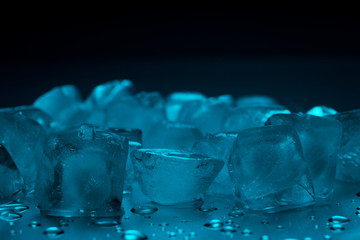 Ice cubes in turquoise color on a black background with drops of water