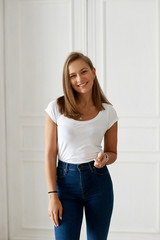 Fototapeta na wymiar Young beautiful pretty woman standing and posing against white wall. Female wearing blue jeans and white t-shirt. Lifestyle portrait