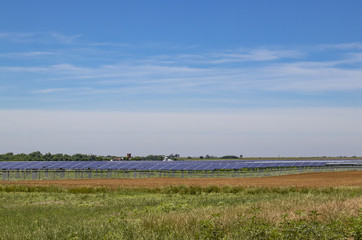 Fototapeta na wymiar Large solar farm out on the plains with a low horizon and farm in distance under pretty blue sky
