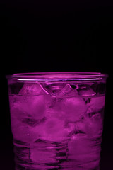 Glass with ice cubes in purple on a black background