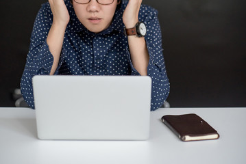 Young Asian businessman dressed in casual style thinking and working with laptop computer on modern desk in office workspace. urban lifestyle and technology concepts