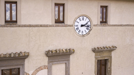 Fototapeta na wymiar Detail of a clock hanging on the facade of a building. The clock, belonging to the 800's, is located between two windows and continues to set the time and dictate the time to the town.