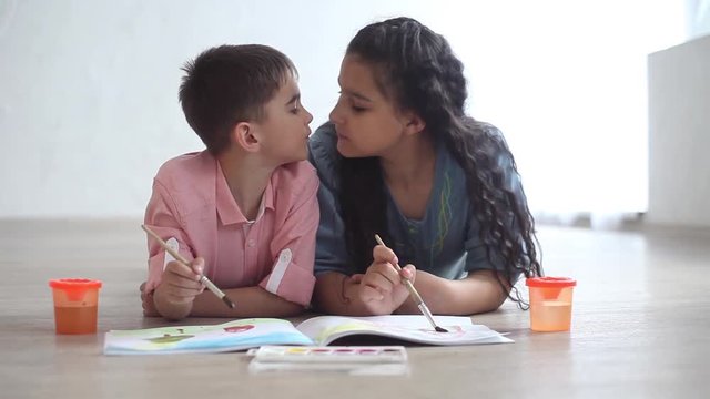 Little boy and little girl paint with paint on album lying on the floor