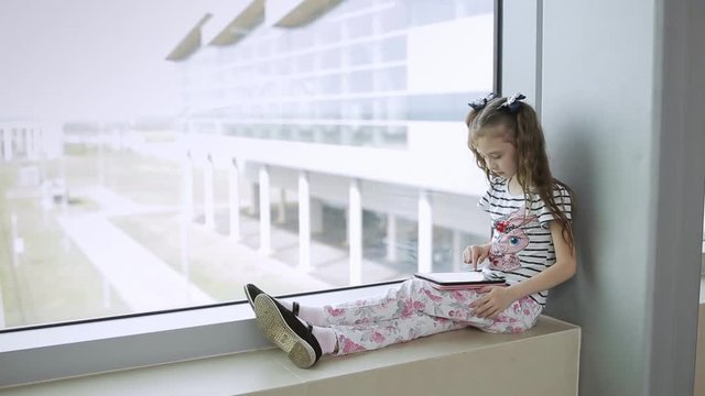 Child at the airport near the window playing a game on the tablet and waiting for time of flight