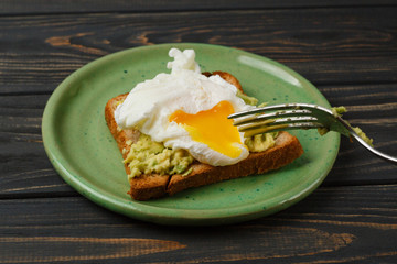 Toast and poached egg with avocado on a green plate on wooden table