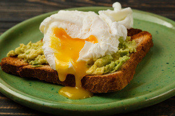 Toast and poached egg with avocado on a green plate on wooden table