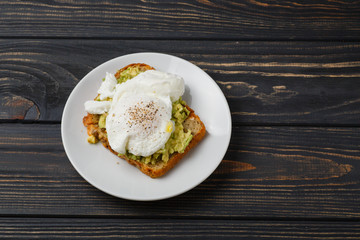 Toast and poached egg with avocado on a plate on wooden table
