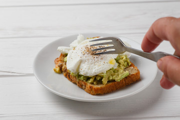 Toast and poached egg with avocado on a plate on white wooden table
