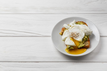 Toast and poached egg with avocado on a plate on white wooden table