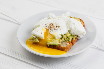 Toast and poached egg with avocado on a plate on white wooden table