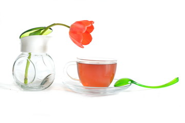 elegant curved green spoon on saucer, glass transparent cup of hot black tea and blooming red Tulip flower in sugar bowl on a white background for morning home relax