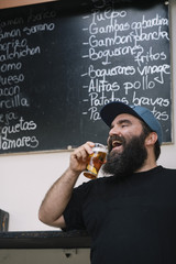 Bearded man with beer next to the typical bar poster in Madrid