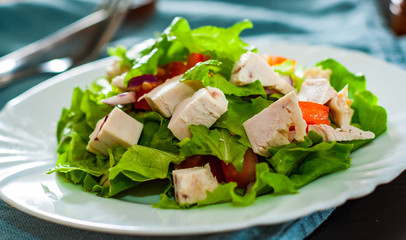 fresh vegetables salad with chicken and onion, lettuce, tomato in white plate on table
