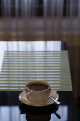 Cup of fresh coffee on a saucer and spoon on table.