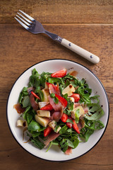 Strawberry, basil, mint, arugula salad with brie cheese and jamon on white plate on wooden table. vertical, overhead