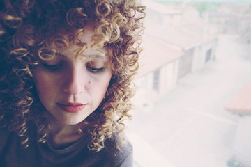 Retrato de una bonita mujer rubia con el pelo rizado apoyada en una ventana de su casa