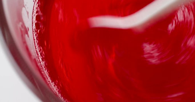 Video of stirring strawberry flavor gelatin in a bowl of water with a white plastic spoon.