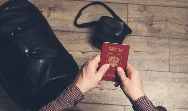 Man sitting holds Russian travel passport in hands with leather bag and photo camera on the floor. Travel and tourism concept.