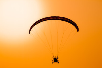 Paraglider flying with paramotor on dramatic sunset sky with big sun in orange and yellow. Concept for adventure extreme ultra light aviation 