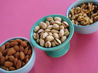 Healthy nuts in blue and green bowls on pink background, almonds, pistachios in the shell, and walnuts