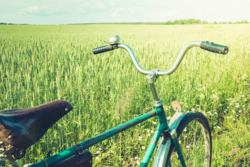 Fototapeta na wymiar Vintage bicycle with leather brown saddle. Summer day for trip. View of wheat field. Outdoor.