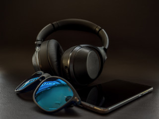 digital native Smartphone and Headphones on dark leather surface with sunglasses