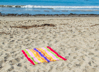 colorful striped beach towel spread out at an empty beach on a sunny summer day with the ocean in the distance