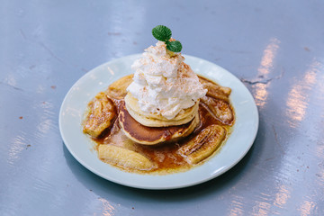 Pancakes with caramel-banana syrup topping with whip cream and mint leaves.