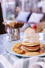 Pancakes with caramel-banana syrup topping with whip cream and mint leaves. In blue plate over fabric with blue stripes.