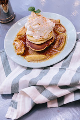 Top view of Pancakes with caramel-banana syrup topping with whip cream and mint leaves. In blue plate over fabric with blue stripes.