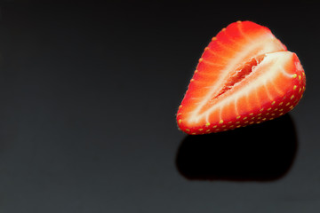 Halve of a strawberry on a reflective black background.