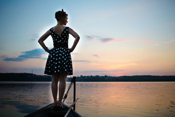 A beautiful young woman dressed standing by the lake, on the background of the sunset