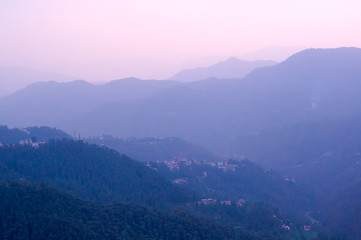 Fototapeta premium Blue hills with trees on them fading into the distance and the pink glowing sky of dusk shot in shimla. Showcases the tranquility and beauty of the place
