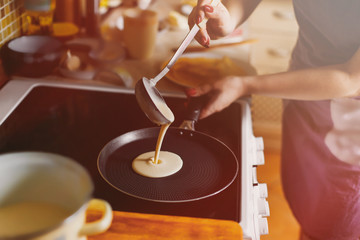 Fototapeta na wymiar Cooking pancakes. In kitchen on a round skillet liquid dough from the ladle is poured