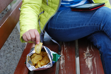 The girl is reading an e-book and eating chips.