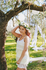 Naklejka premium Attractive young girl sits in a park near a tree. Blond girl in free city clothes.