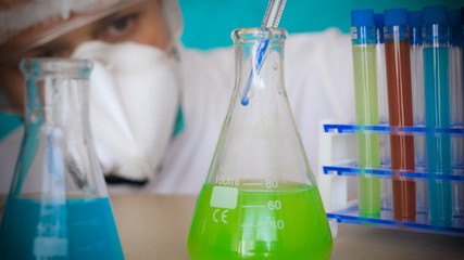The alchemist, holds the flasks, tests the test tubes with a test of different compositions, in a white coat, a respirator, goggles, rubber white gloves, a green background.