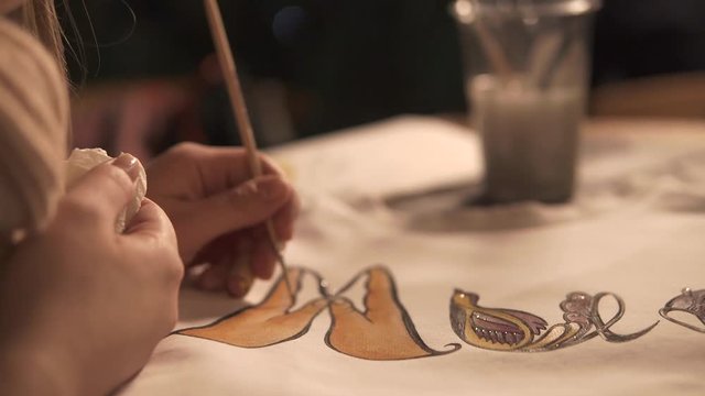 Female artist is making batik patterns on a white sweatshirt in studio. Close-up of her hands, craft production of designer clothes
